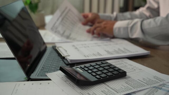 Accountant using calculator with financial documents during tax season for tax preparation, accounting, audit, bookkeeping, financial planning.