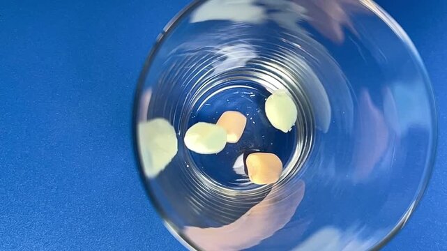 Pastel marshmallows are falling into clear glass against blue background, showing colorful pieces dropping into container