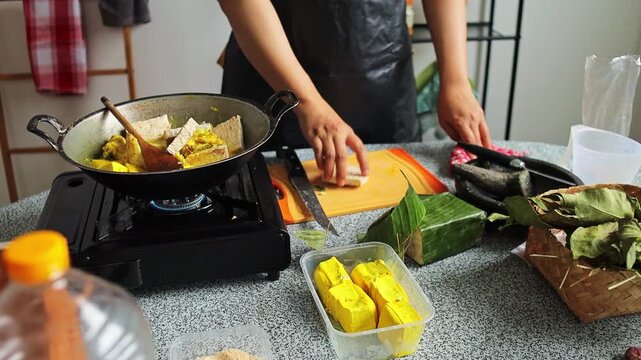Chef adds sliced tempeh to wok simmering chicken soup and stirs gently with wooden spoon