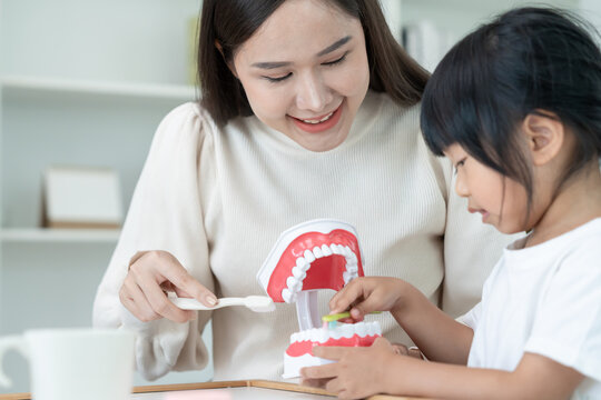 Mother teaching asian girl use toothbrush to clean, suffers from pain in tooth. Teeth decay, dental problems, tooth brushing practice, oral health care, reducing sweets, fluorine coating