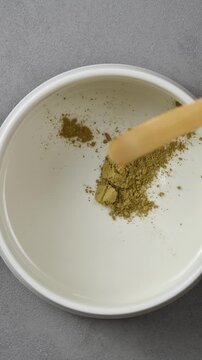 Hojicha powder is added from wooden spoon into ceramic bowl during traditional Japanese tea preparation in vertical closeup.