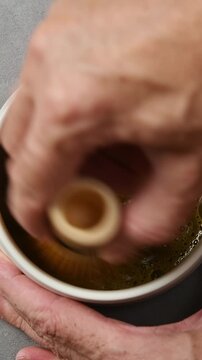 Hojicha tea is whisked with bamboo chasen in ceramic bowl until foam forms during vertical closeup Japanese tea preparation.