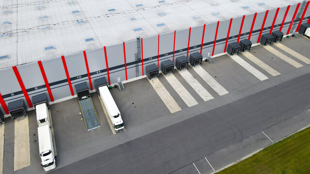 Modern logistics center with semi trucks backing up and preparing for cargo loading or unloading at multiple dock bays, highlighting global distribution and supply chain operations