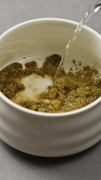 Hot water is poured over hojicha powder in ceramic bowl, beginning traditional preparation of roasted Japanese tea drink.