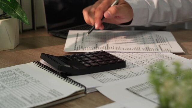 Close up accountant hand using calculator on financial reports during tax season for accounting, tax preparation, audit, bookkeeping, financial planning.