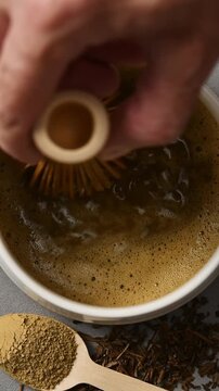Bamboo whisk quickly froths hojicha in ceramic bowl, with powder and roasted leaves shown in vertical macro closeup detail.