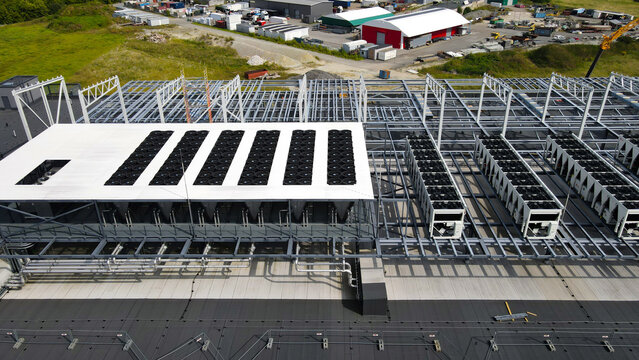 Aerial view capturing a data center rooftop undergoing construction, with large scale cooling units and structural framework being installed, highlighting technological expansion