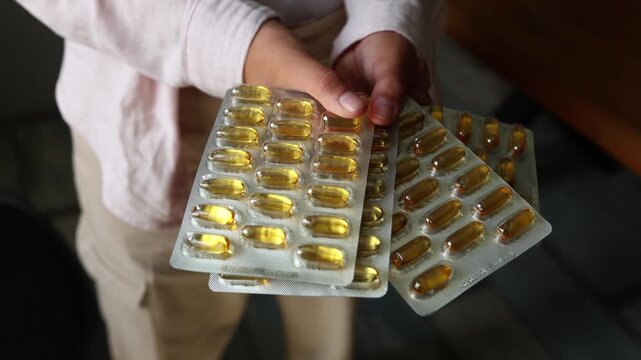 A person shows a tray filled with fish oil capsules in a room during daytime. The focus is on the importance of omega-3 for health.