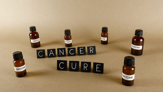 Black letter tiles spelling CANCER CURE surrounded by vaccine bottles, symbolizing research and scientific progress in developing a treatment or prevention for the disease