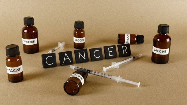 Cancer word spelled out with letter tiles surrounded by vaccine bottles and syringes, representing research, treatment, and the global fight against disease