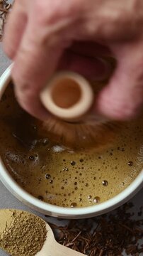 Hand slowly whisks hojicha in ceramic bowl, showing smooth foamy texture during traditional Japanese roasted tea preparation.
