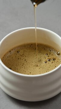Syrup pours into foamy hojicha in white ceramic bowl, adding sweetness during traditional Japanese tea drink preparation.
