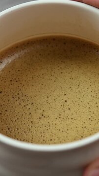 Hands gently rotate ceramic bowl in small circles, revealing smooth foamy hojicha texture during Japanese tea preparation.