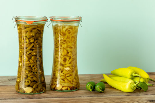 Two jars of Asian-style pickled chilies of two varieties: Jalapeno and Hungarian Hot Wax, with fresh chilies next to them. Copy space.
