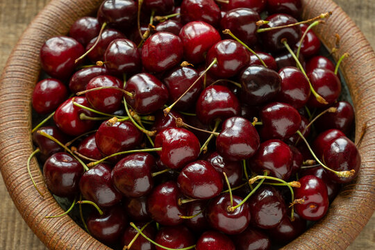 Top view of sweet cherries with stems on a handmade ceramic plate. Fresh organic fruit on a vintage ribbed dish; top view, backlit by natural light.