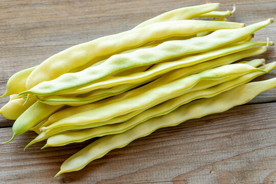 Merveille de Venise yellow pole beans on a rustic wooden background. Fresh organic wax bean pods backlit by natural light.