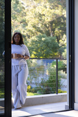 Adult African woman standing on balcony with watch holding ceramic mug near railing, copy space © WavebreakMediaMicro