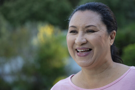 Mature African American woman smiling and laughing in garden in light pink top and stud earrings
