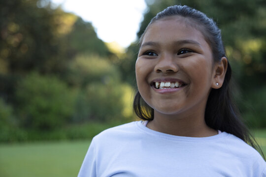 African American child smiling, standing in grassy park wearing white tee, stud earring, copy space