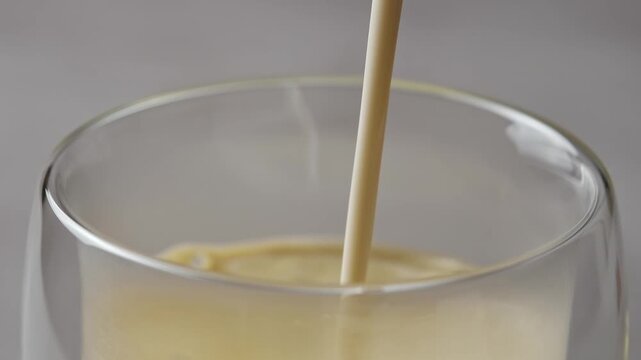 Oat milk pours into hojicha latte in clear glass, blending with roasted tea and forming silky foam in detailed close-up view.