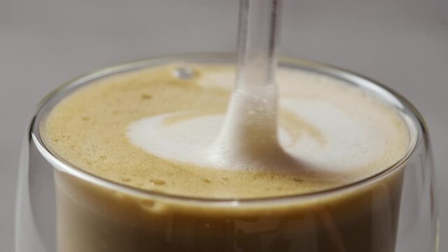 Glass straw slowly stirs creamy hojicha oat milk latte, blending silky foam across surface in detailed horizontal closeup.