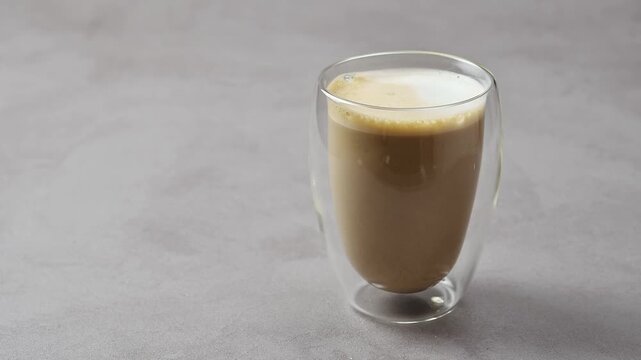Finished hojicha oat milk latte stands in clear double wall glass on gray table with copy space for beverage advertising.