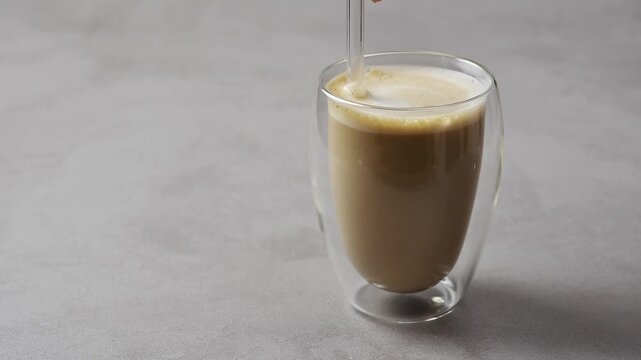 Glass straw stirs hojicha oat milk latte in clear glass, blending creamy foam while leaving copy space for beverage ads.
