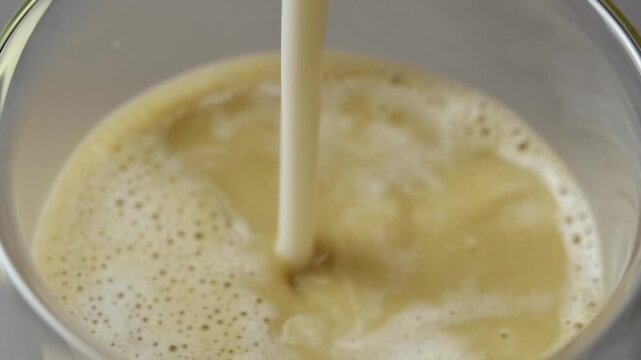 Close up oat milk pours into roasted hojicha tea in a glass, creating creamy foam during preparation of a dairy free latte.