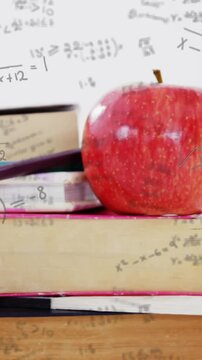 Mathematical equations moving against stack of books and apple