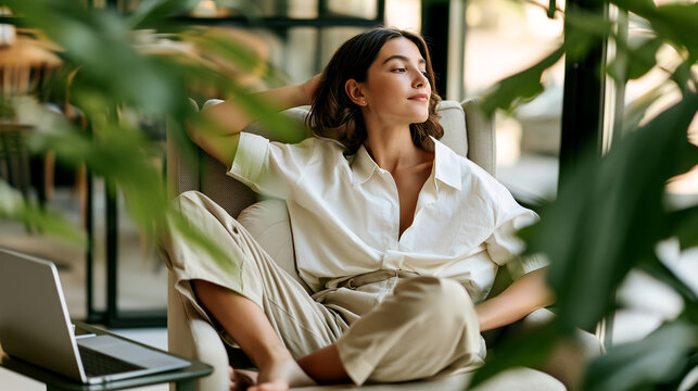 Woman relaxes in an armchair with a supportive lumbar cushion while working remotely, illustrating ergonomic posture, back health, and a calm home-office lifestyle.