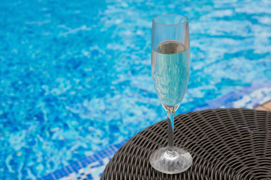 A glass of champagne on a table by a swimming pool.