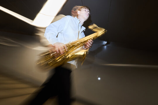 Young adult Caucasian man walking with saxophone in underpass with motion blur, representing street musicians and urban culture. Ideal for music event promotion, low angle shot