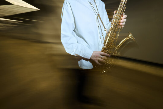 Caucasian young adult male street musician playing saxophone with motion blur effect, representing urban culture and live performance. Ideal for music festival promotion