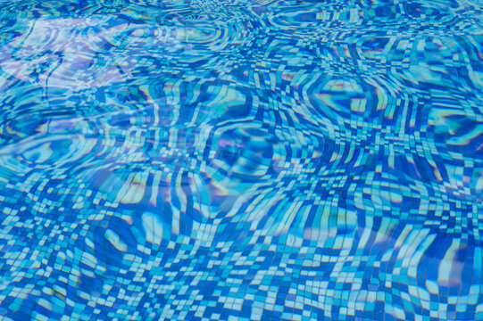 Blurry rippled blue water in a swimming pool with mosaic tile bottom.
