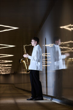 Vertical shot of young adult Caucasian man playing saxophone in urban underpass, performing as street musician. Image suitable for music education and cultural event promotion