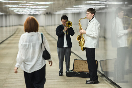 Young Caucasian male street musicians playing saxophone and trombone in underground pedestrian tunnel. Image represents urban culture and is suitable for city lifestyle marketing