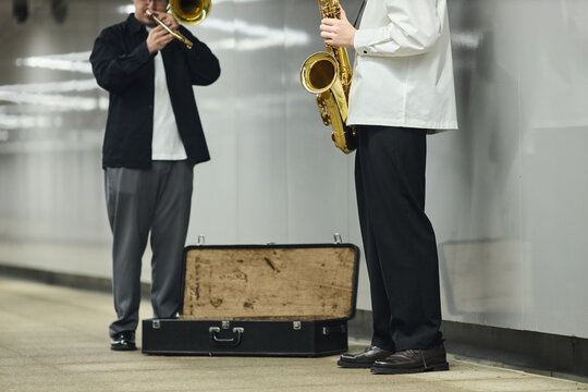 Two young adult Caucasian male street musicians playing saxophone and trombone in subway station. Image suitable for urban culture articles and music event promotion, eye level shot