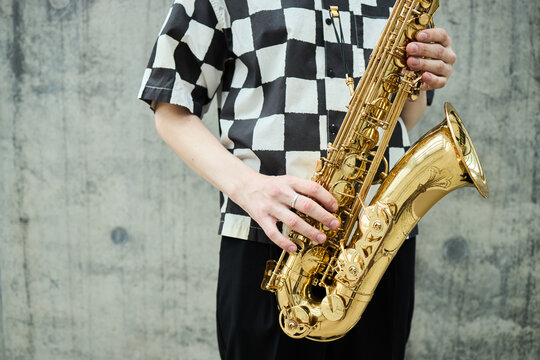 Midsection of young adult Caucasian street musician holding saxophone outdoors. Image representing urban culture and live performance, suitable for music festival promotion, medium shot
