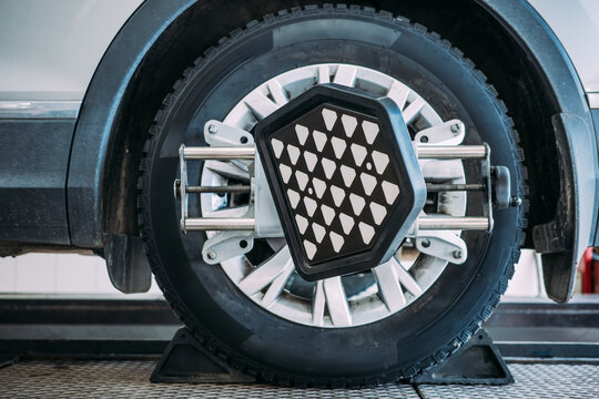 Studded winter tire on SUV during alignment check, front wheel on service platform for seasonal preparation, improved grip, safe driving, automotive maintenance and diagnostics.