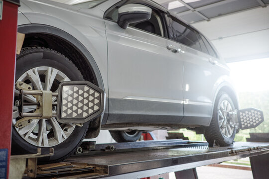 Wheel alignment SUV service in auto workshop, vehicle on lift with optical targets for suspension diagnostics, steering geometry adjustment, maintenance and road safety.