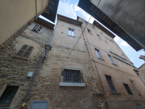 Ripresa verticale dal basso di storici edifici in pietra e mattoni che si stagliano contro il cielo in un vicolo medievale italiano