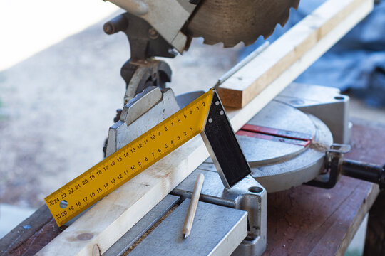 Carpentry workshop with a miter saw, wooden planks, ruler and carpenter pencil prepared for cutting and measuring lumber during a woodworking project.