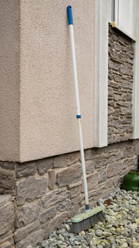 Outdoor broom leaning against stone wall on pebble ground