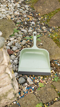 Green dustpan on pebble and stone path in garden setting