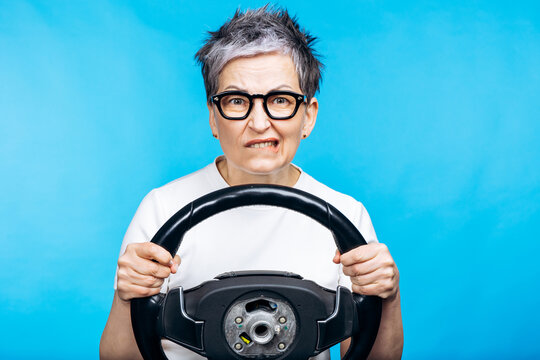 Mature woman driver experiencing stress and apprehension, biting her lip, holding a steering wheel against a blue background