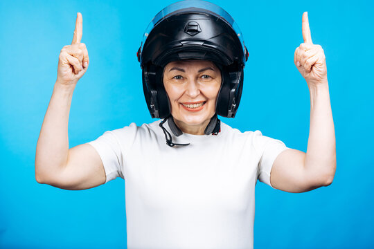Happy senior woman wearing a motorcycle helmet and pointing both index fingers up, promoting safety and protection