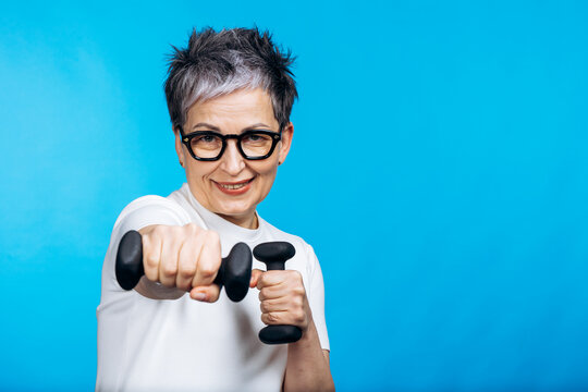 Senior woman smiling and actively training with small weights, promoting healthy aging, fitness, and vitality on a blue background