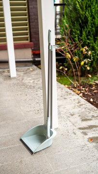 Dustpan and broom on outdoor patio with greenery in background