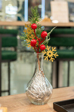 Festive glass vase with pine branches, red berries, and golden snowflakes