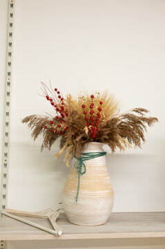 Rustic vase with dried flowers and red berries on wooden shelf